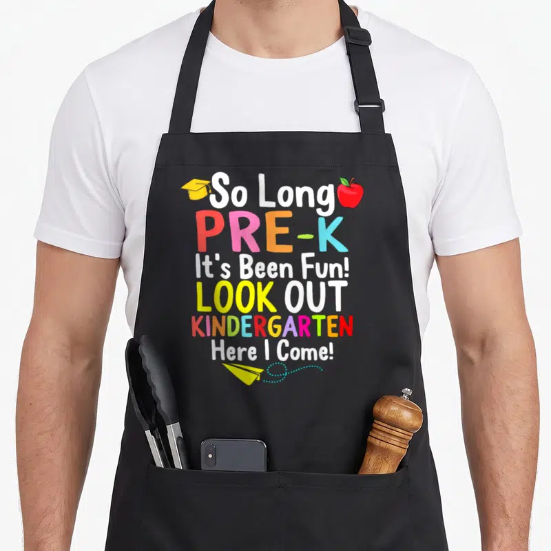 Kindergarten come and get it apron - Stacked colorful text So Long Pre-K with graduation cap, red apple, and paper — shown on a black cotton canvas apron against a white background