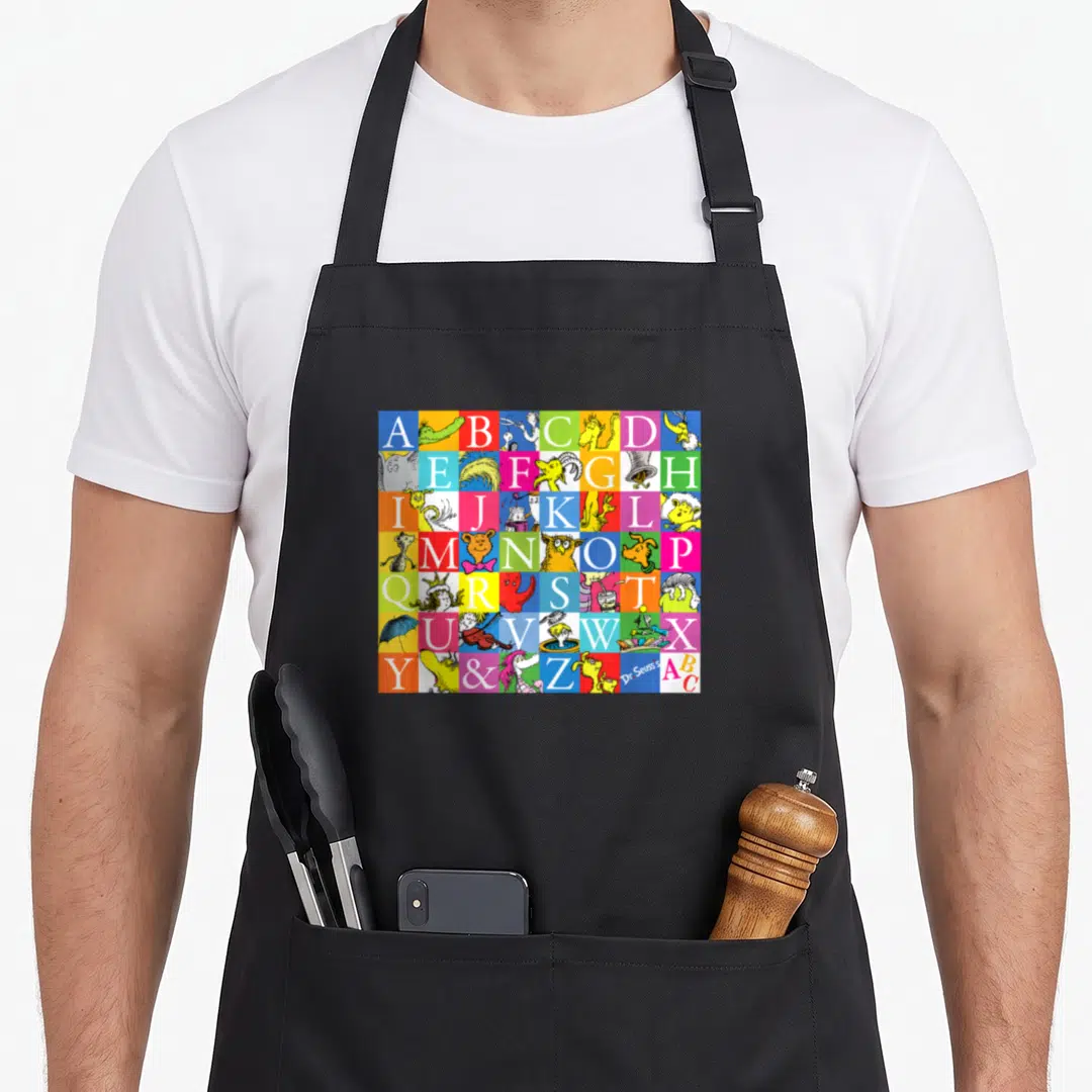 Funny z apron - Colorful alphabet grid with cartoon creatures and Dr Seuss signature — shown on a black cotton canvas apron against a white background