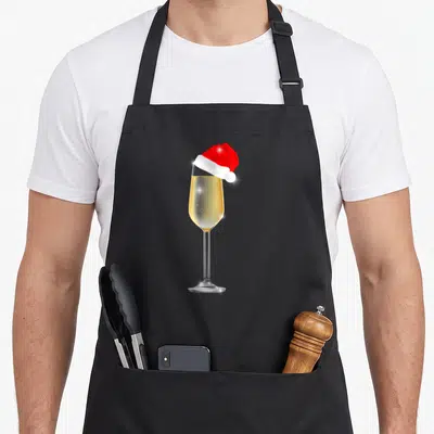 Christmas champagne apron - Realistic champagne glass with yellow liquid and red white santa hat — shown on a black cotton canvas apron against a white background