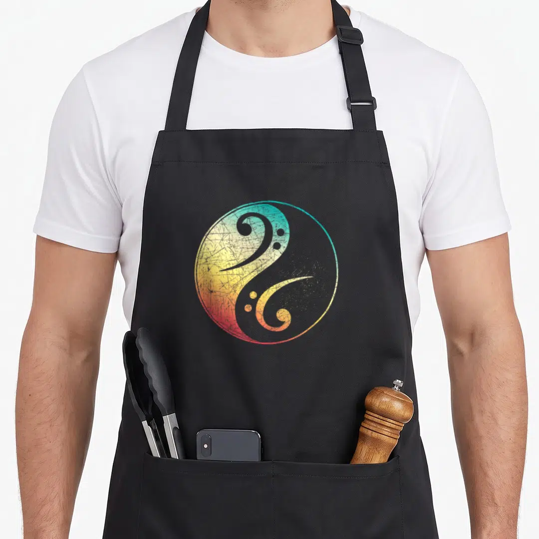 Musical bass apron - Retro yin yang symbol with bass clef curves in blue yellow red and grey — shown on a black cotton canvas apron against a white background