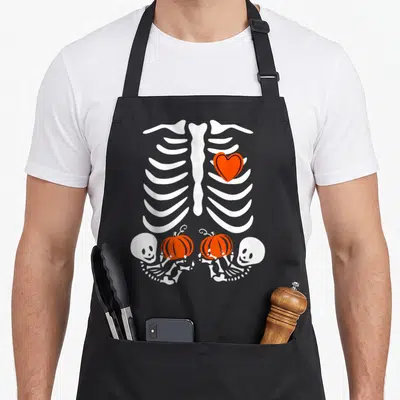 Twin halloween apron - White ribcage with orange heart and two skeletons holding orange pumpkins — shown on a black cotton canvas apron against a white background