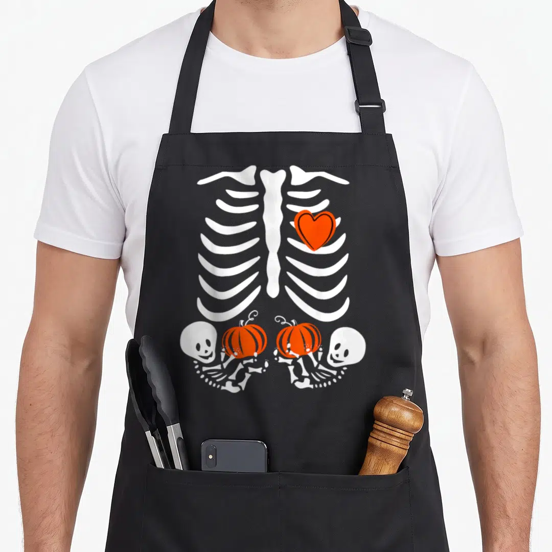 Twin halloween apron - White ribcage with orange heart and two skeletons holding orange pumpkins — shown on a black cotton canvas apron against a white background