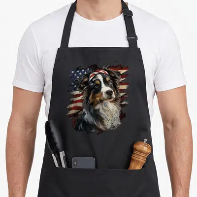 Patriotic australian aprons - Realistic dog head wearing a patriotic headband in front of a distressed American flag — shown on a black cotton canvas apron against a white background