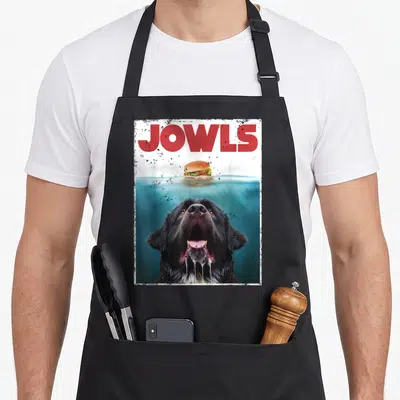 Newfoundland newfie dog apron - JOWLS text above black dog underwater gazing at floating hamburger in red blue black — shown on a black cotton canvas apron against a white background