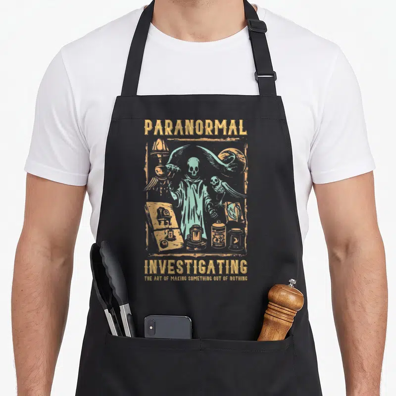 Hunting investigator ghost apron - Gold and mint green line art of a skeleton with occult tools and text PARANORMAL — shown on a black cotton canvas apron against a white background