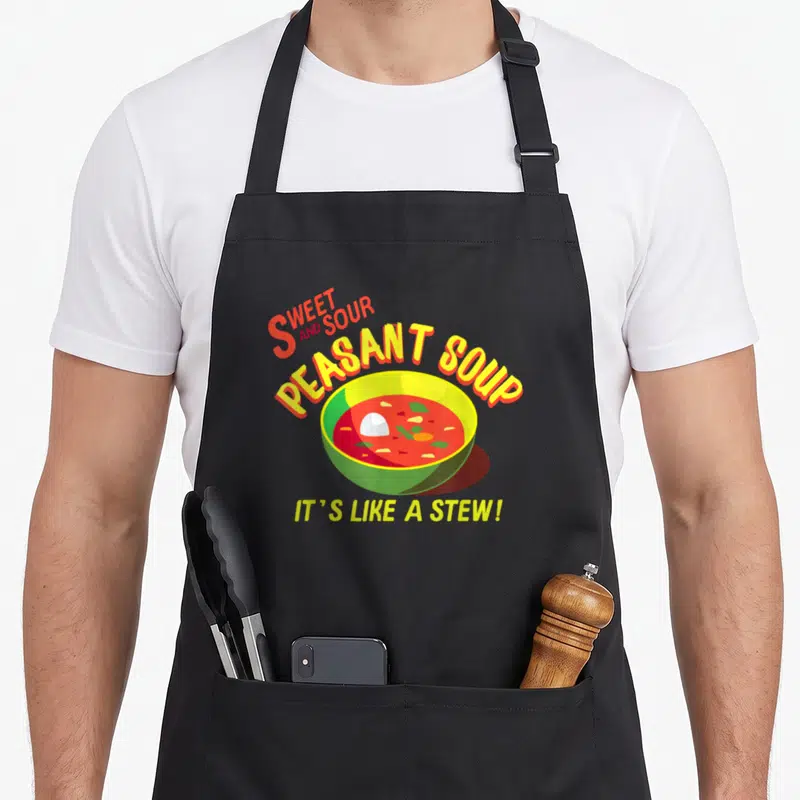 Sweet soup lovers apron - Bowl of red soup with green rim and yellow text reading sweet and sour peasant soup — shown on a black cotton canvas apron against a white background