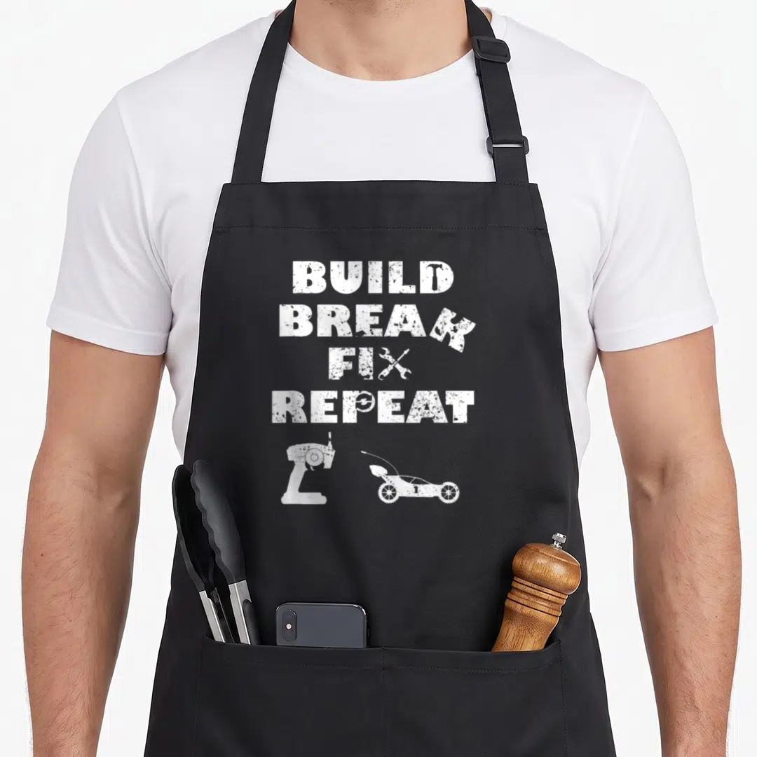 Fix car apron - White distressed BUILD BREAK FIX REPEAT text with hammer wrench bench grinder and go-kart silhouettes — shown on a black cotton canvas apron against a white background