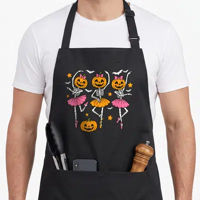 Ballet skeleton halloween apron - Three skeleton ballerinas with pumpkin heads in pink and orange tutus with bats — shown on a black cotton canvas apron against a white background