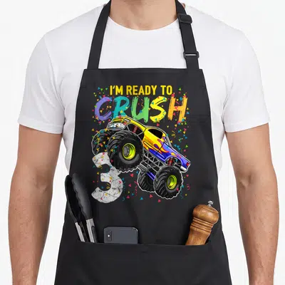 Birthday age truck apron - I'm ready to crush 3 monster truck with confetti and multi-colored letters — shown on a black cotton canvas apron against a white background