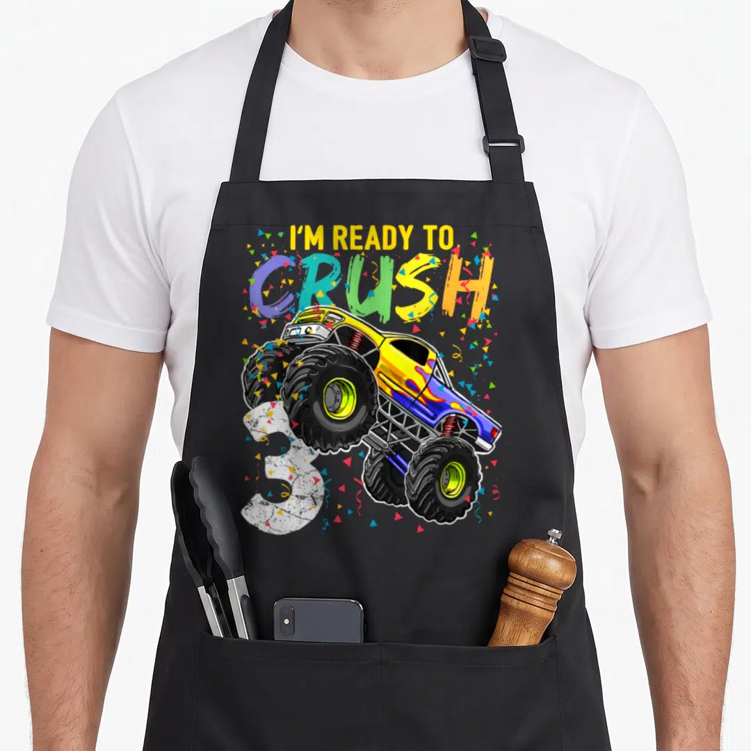 Birthday age truck apron - I'm ready to crush 3 monster truck with confetti and multi-colored letters — shown on a black cotton canvas apron against a white background