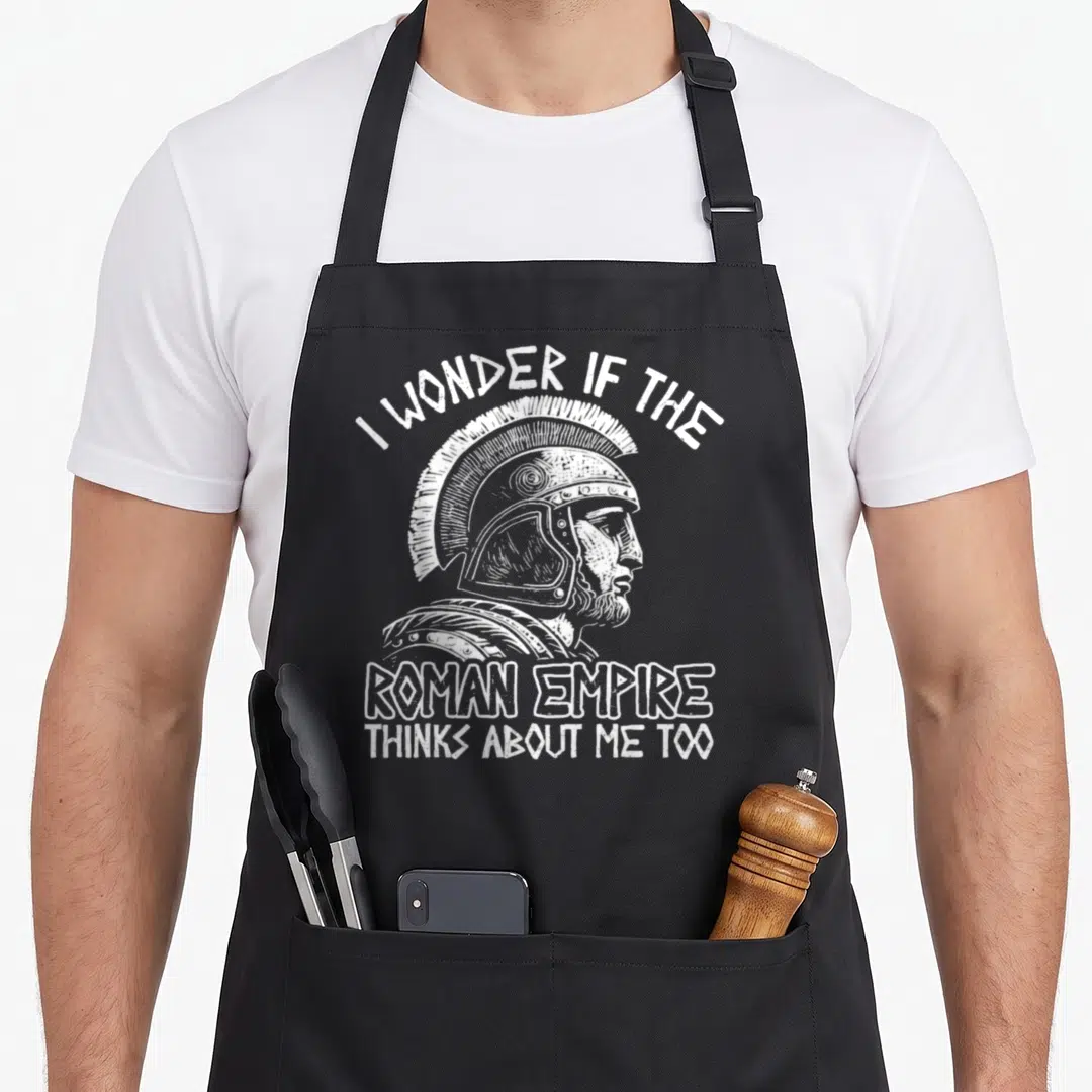 Empire italy apron - White distressed Roman soldier profile with arched text reading I WONDER IF THE ROMAN EMPIRE — shown on a black cotton canvas apron against a white background