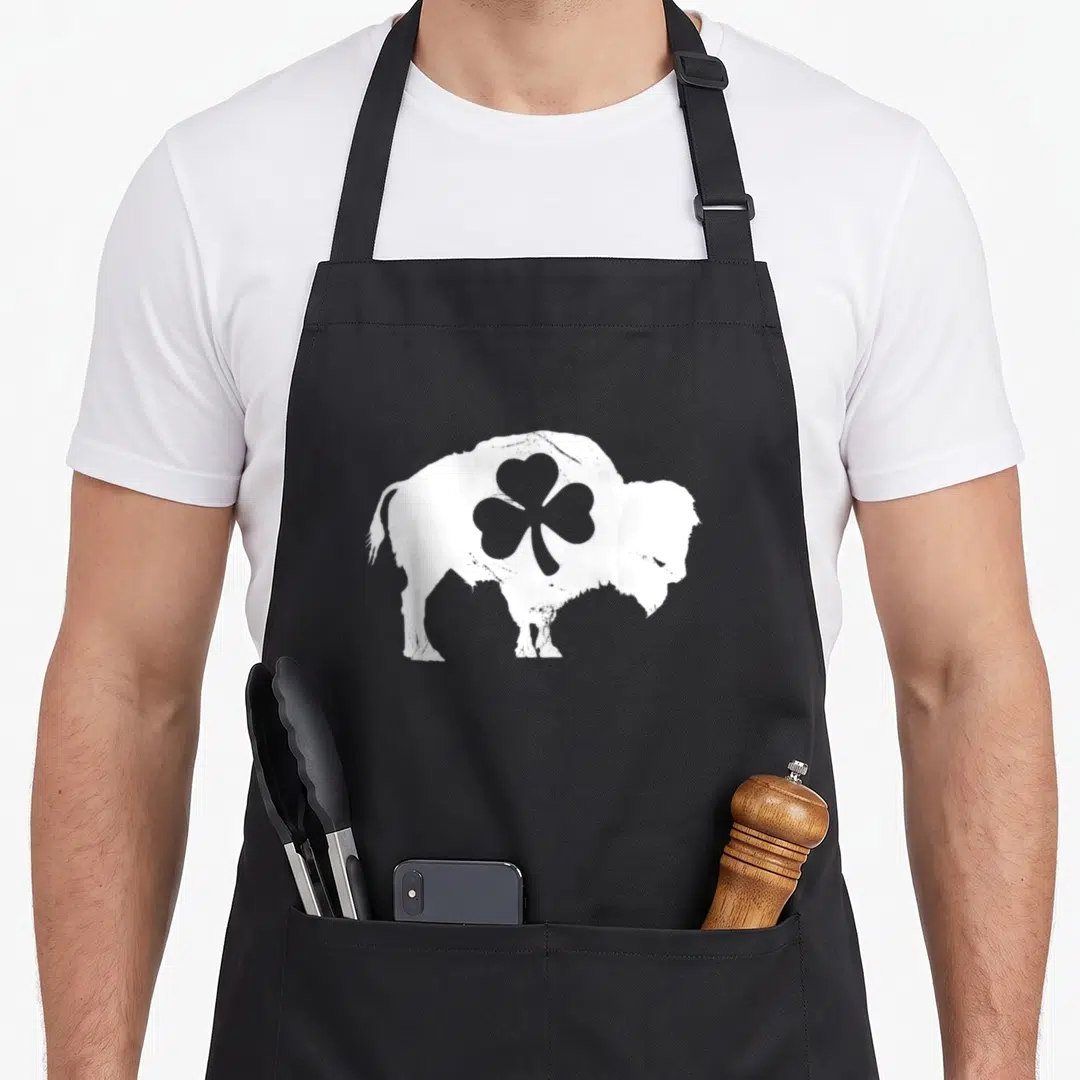 Buffalo st patrick day aprons - White bison silhouette with grey shamrock cutout in center, minimalist style — shown on a black cotton canvas apron against a white background