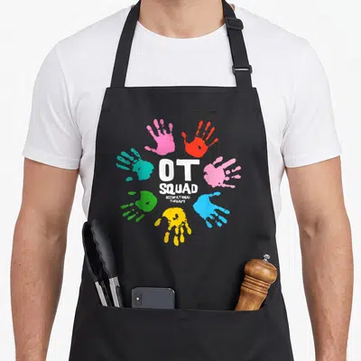 Squad occupational ot apron - Seven colorful handprints circle white OT SQUAD OCCUPATIONAL THERAPY text — shown on a black cotton canvas apron against a white background
