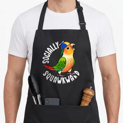 Socially pineapple apron - Cartoon parrot in colorful cap with white arched text reading SOCIALLY SQUAWKWARD — shown on a black cotton canvas apron against a white background