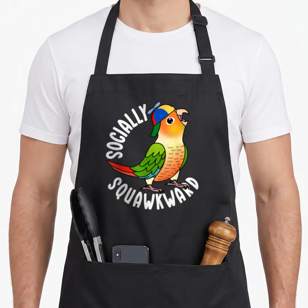 Socially pineapple apron - Cartoon parrot in colorful cap with white arched text reading SOCIALLY SQUAWKWARD — shown on a black cotton canvas apron against a white background