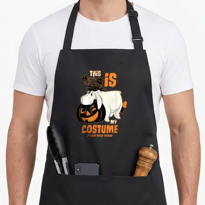 Eeyore halloween apron - Cartoon donkey leaning on orange pumpkin with text THIS IS MY COSTUME IT'S NOT MUCH THOUGH — shown on a black cotton canvas apron against a white background