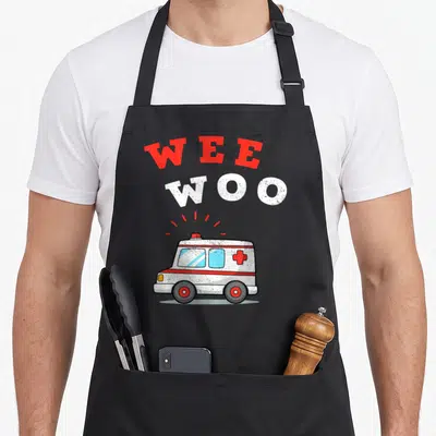 Wee emt apron - Cartoon ambulance with stacked Wee Woo text in red and white on grey background — shown on a black cotton canvas apron against a white background