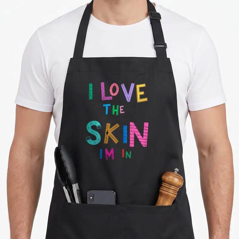 Skin african american aprons - I Love The Skin Im In colorful stacked typography design — shown on a black cotton canvas apron against a white background