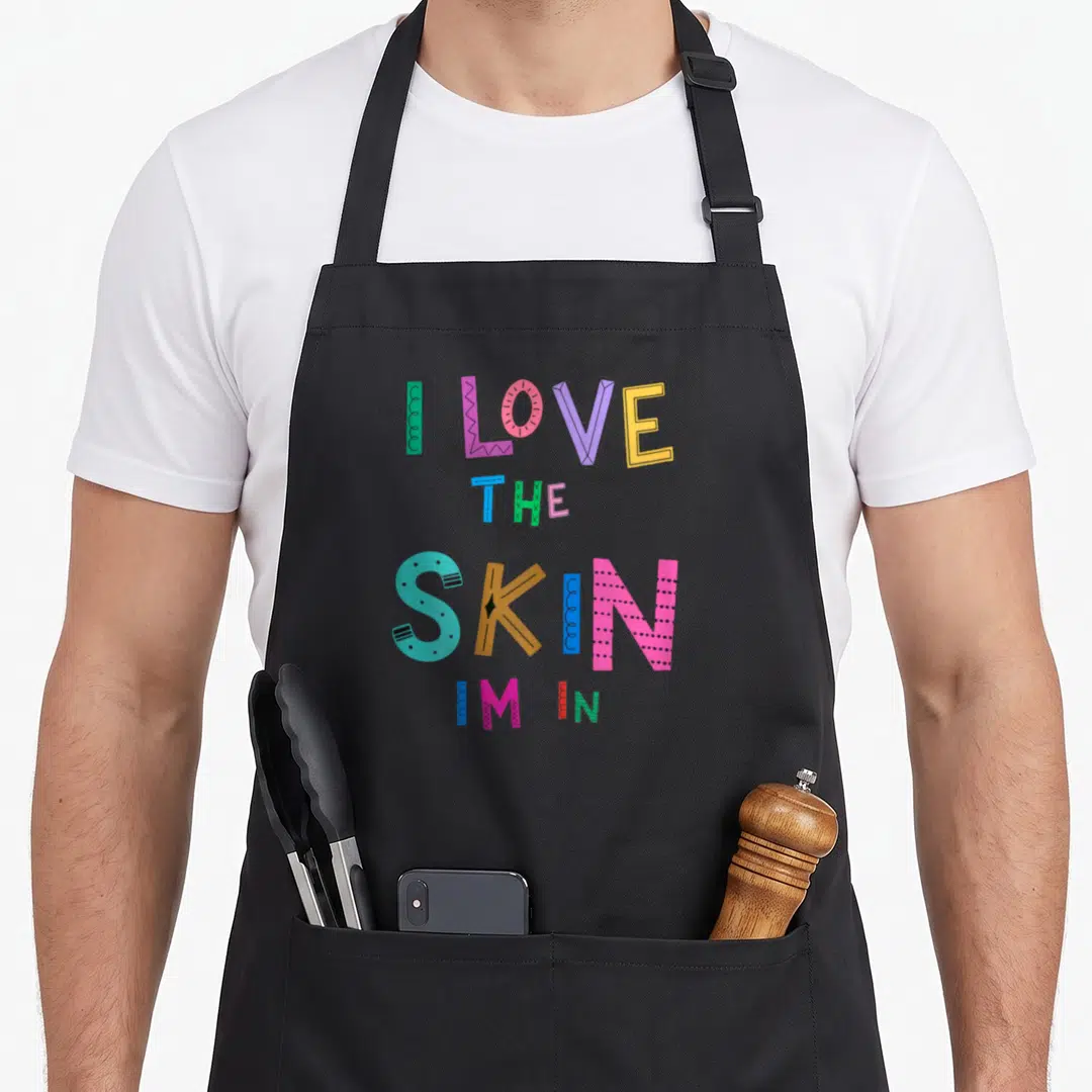 Skin african american aprons - I Love The Skin Im In colorful stacked typography design — shown on a black cotton canvas apron against a white background