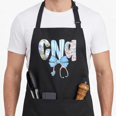 Coquette floral apron - CNA letters with floral patterns, blue bow, and pink stethoscope — shown on a black cotton canvas apron against a white background
