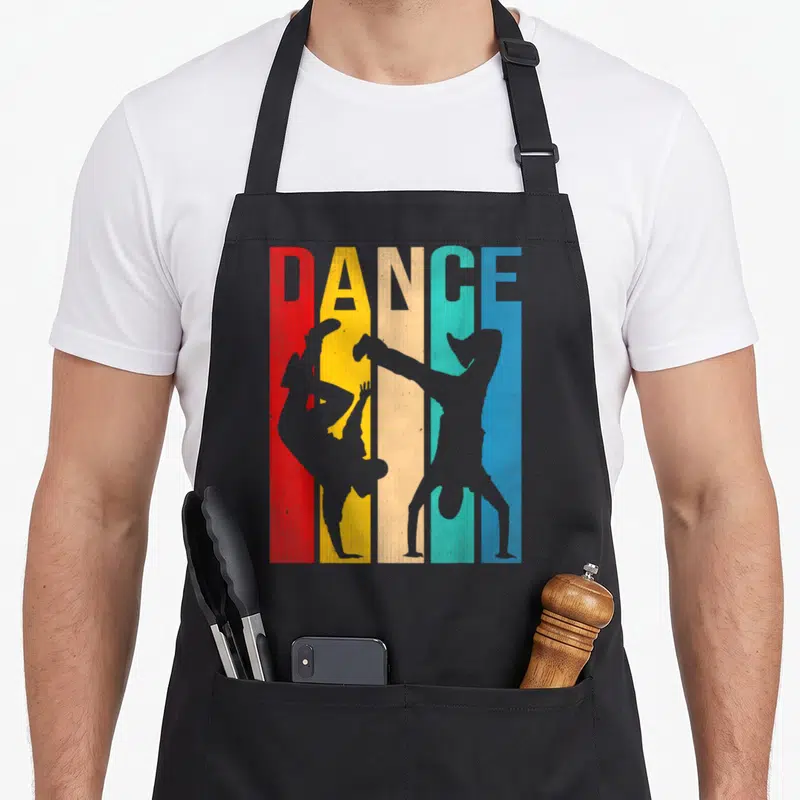 Breakdancing dancer apron - DANCE text above five red yellow teal blue grey vertical stripes with two grey dancer — shown on a black cotton canvas apron against a white background