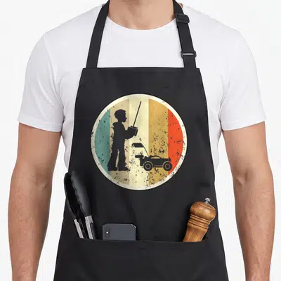 Model car apron - Grey silhouette of boy holding remote control car over red orange yellow green stripes — shown on a black cotton canvas apron against a white background