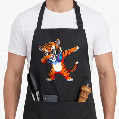 Dabbing tiger animal apron - Cartoon orange tiger dabbing with sunglasses and blue headphones — shown on a black cotton canvas apron against a white background