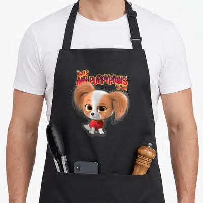Puppypaw junior apron - Arched text That's Mr. Puppypaws To You above a white and brown dog in a red sweater surrounded — shown on a black cotton canvas apron against a white background