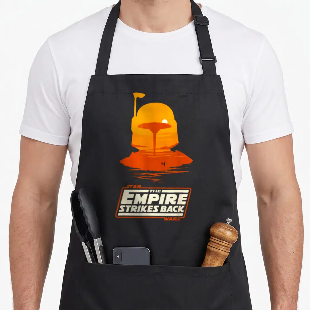 Empire boba apron - Orange helmet silhouette containing a landscape scene above Star Wars Empire Strikes Back text logo — shown on a black cotton canvas apron against a white background