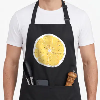 Citrus lemon apron - Distressed yellow lemon slice graphic on black fabric background — shown on a black cotton canvas apron against a white background