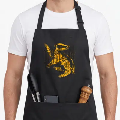 Loyalty hufflepuff apron - Hufflepuff crest with Loyalty Dedication Patience text and badger in yellow and grey — shown on a black cotton canvas apron against a white background