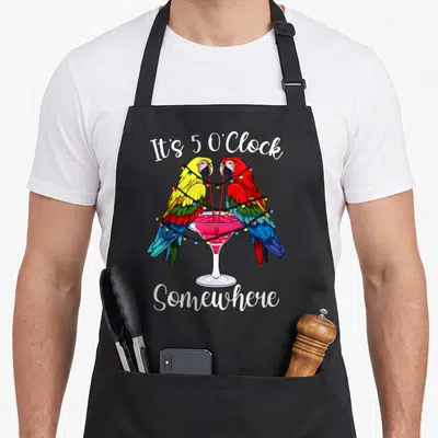 Oclock summer aprons - Two parrots drinking from a pink cocktail glass wrapped in string lights with white text — shown on a black cotton canvas apron against a white background
