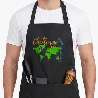 Challenge student aprons - Green world map with orange script and vertical blue text on black fabric — shown on a black cotton canvas apron against a white background