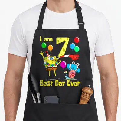 Birthday apron gift - SpongeBob with balloons and I am 7 Best Day Ever text — shown on a black cotton canvas apron against a white background