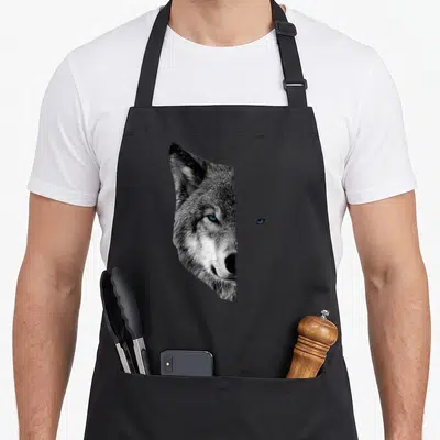 Wolf split apron - Split wolf face portrait with isolated blue eye on black background — shown on a black cotton canvas apron against a white background