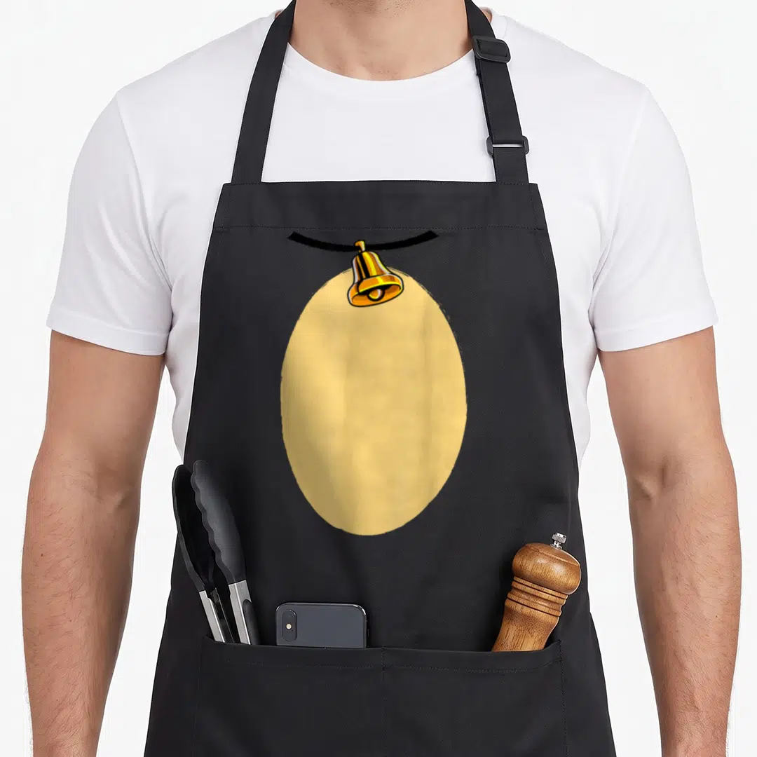 Costume reindeer christmas apron - Gold bell hanging from black ribbon over large beige oval shape — shown on a black cotton canvas apron against a white background
