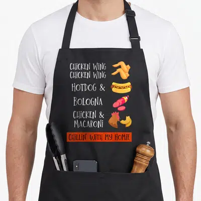 Bologna chicken apron - Cartoon list of chicken wings hotdog bologna and macaroni with Chillin With My Homie text — shown on a black cotton canvas apron against a white background