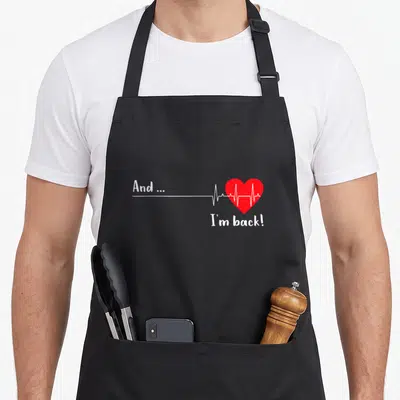 Ekg heartbeat funny apron - White EKG line leading to red heart with text And I'm back on black fabric — shown on a black cotton canvas apron against a white background