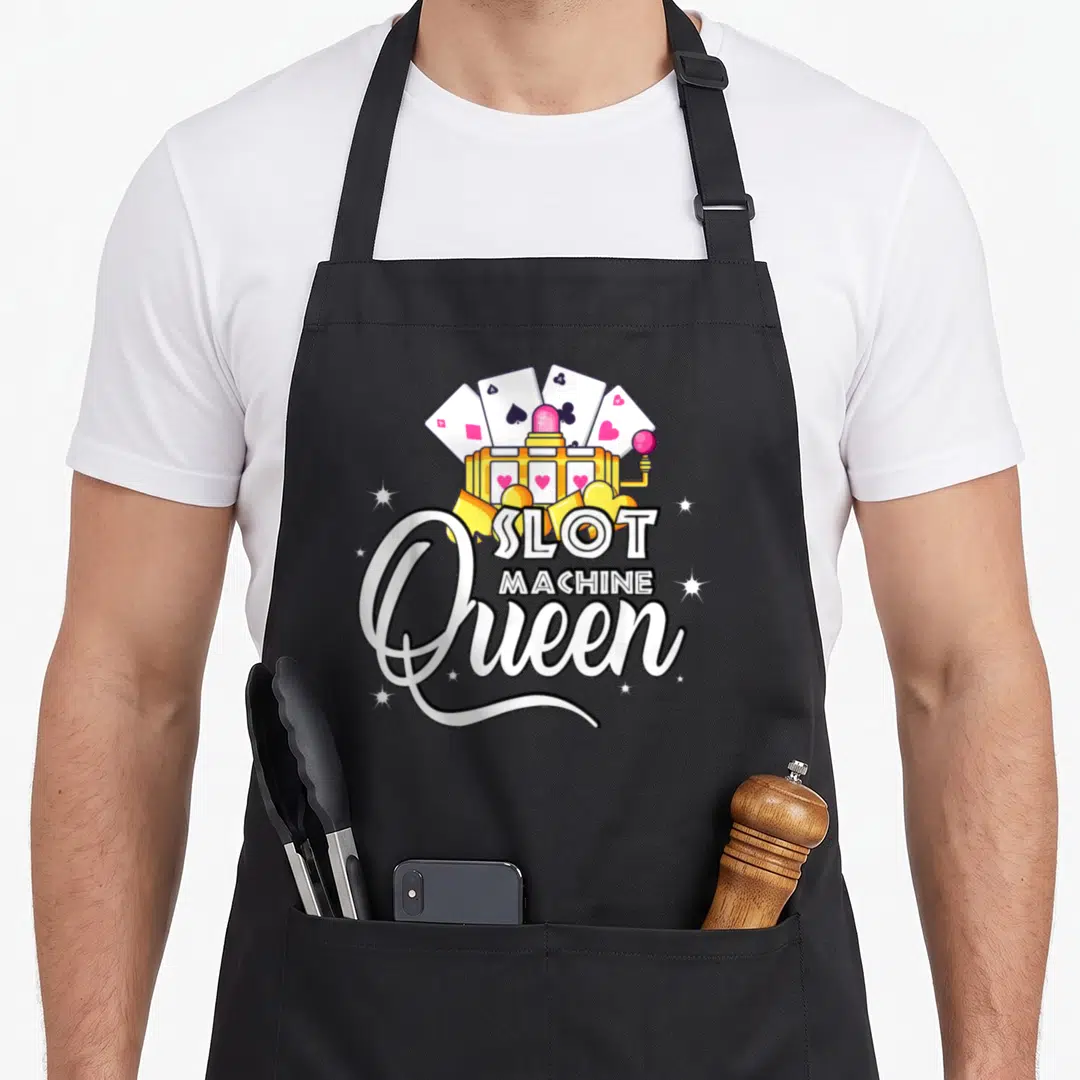 Slot machine apron - Gold slot machine with fanned playing cards and white script text reading Slot Machine Queen — shown on a black cotton canvas apron against a white background