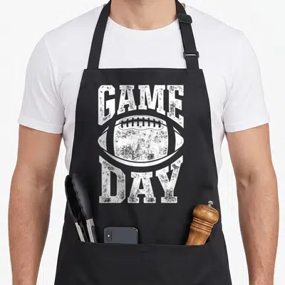 Game sports team aprons - White distressed football graphic with GAME arched above and DAY below — shown on a black cotton canvas apron against a white background