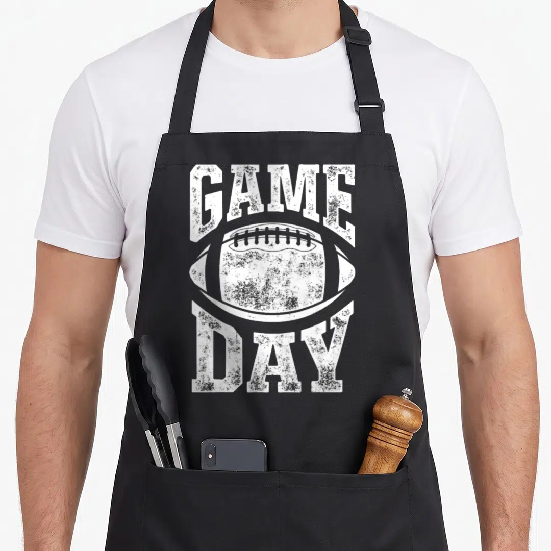 Game sports team aprons - White distressed football graphic with GAME arched above and DAY below — shown on a black cotton canvas apron against a white background