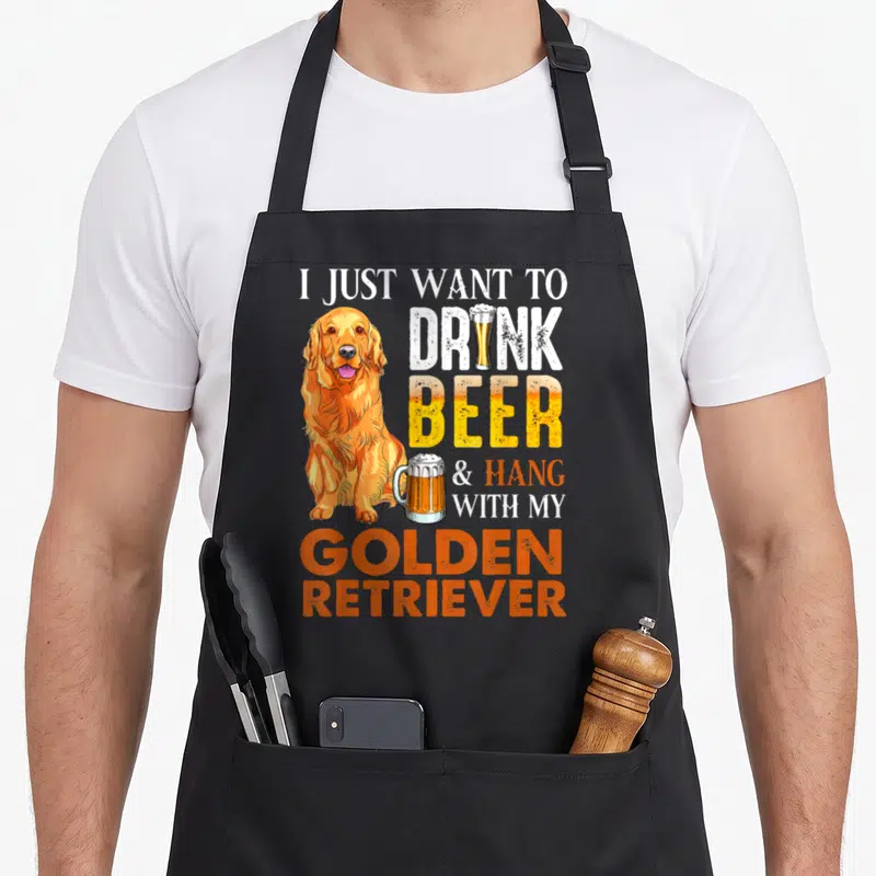 Drink golden retriever apron - Cartoon golden retriever sitting next to stacked text about drinking beer and hanging — shown on a black cotton canvas apron against a white background