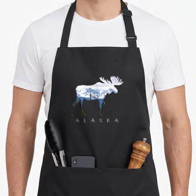 Alaska apron or apron - Moose silhouette filled with snowy mountains and spaced-out ALASKA text below — shown on a black cotton canvas apron against a white background