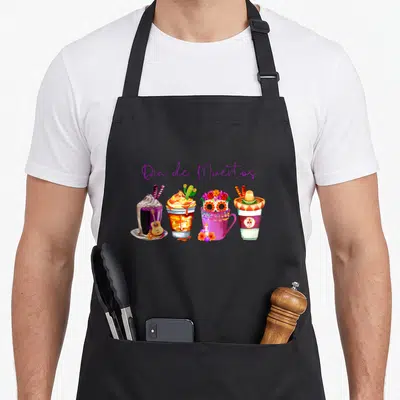 Coffee day of the dead apron - Watercolor drinks with Dia de Muertos text and cultural symbols like guitars and skulls — shown on a black cotton canvas apron against a white background