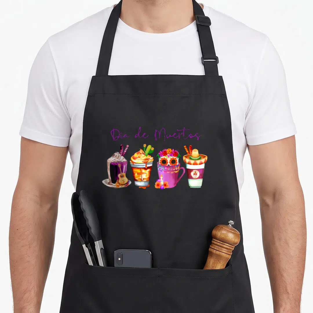 Coffee day of the dead apron - Watercolor drinks with Dia de Muertos text and cultural symbols like guitars and skulls — shown on a black cotton canvas apron against a white background