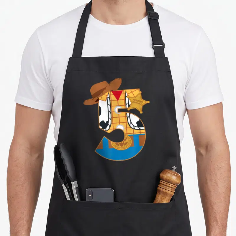 Funny fifth birthday apron - Number 5 cowboy with sheriff star and SHERIFF text in yellow blue brown white — shown on a black cotton canvas apron against a white background