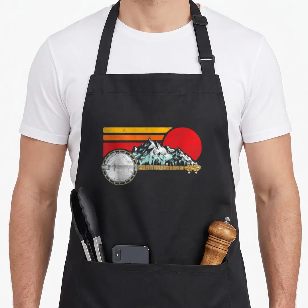 Banjo 80s apron - Retro banjo over teal mountains and red sun with three yellow and white stripes — shown on a black cotton canvas apron against a white background