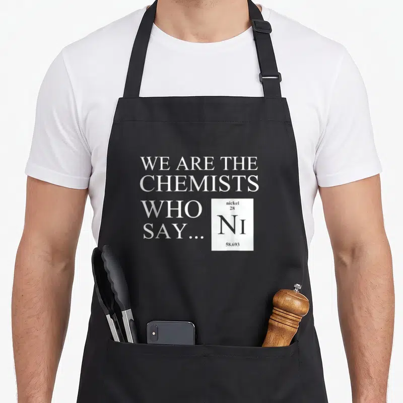 Funny chemist chemistry apron - White text WE ARE THE CHEMISTS WHO SAY next to a nickel element tile on grey — shown on a black cotton canvas apron against a white background