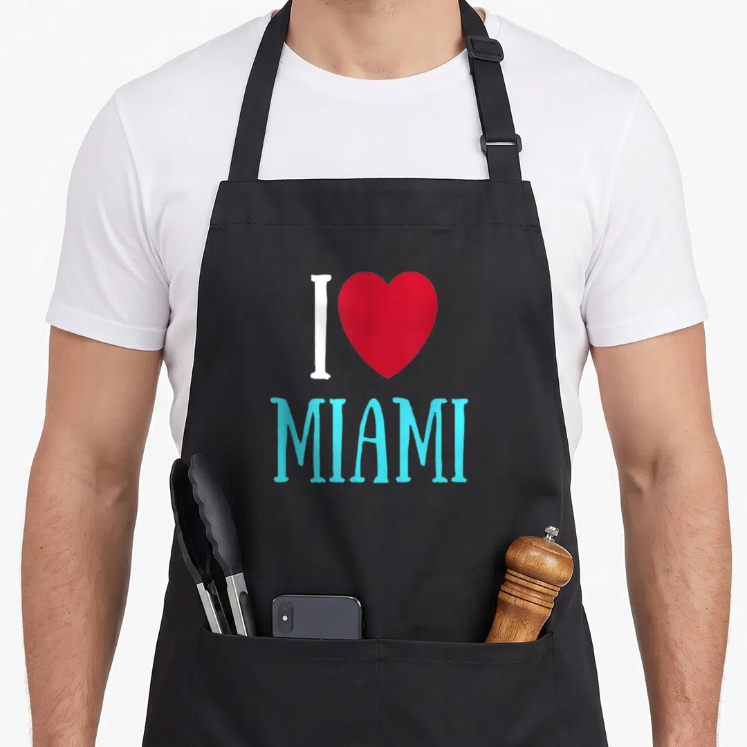 Beach pride apron - White I and red heart above light blue MIAMI text — shown on a black cotton canvas apron against a white background