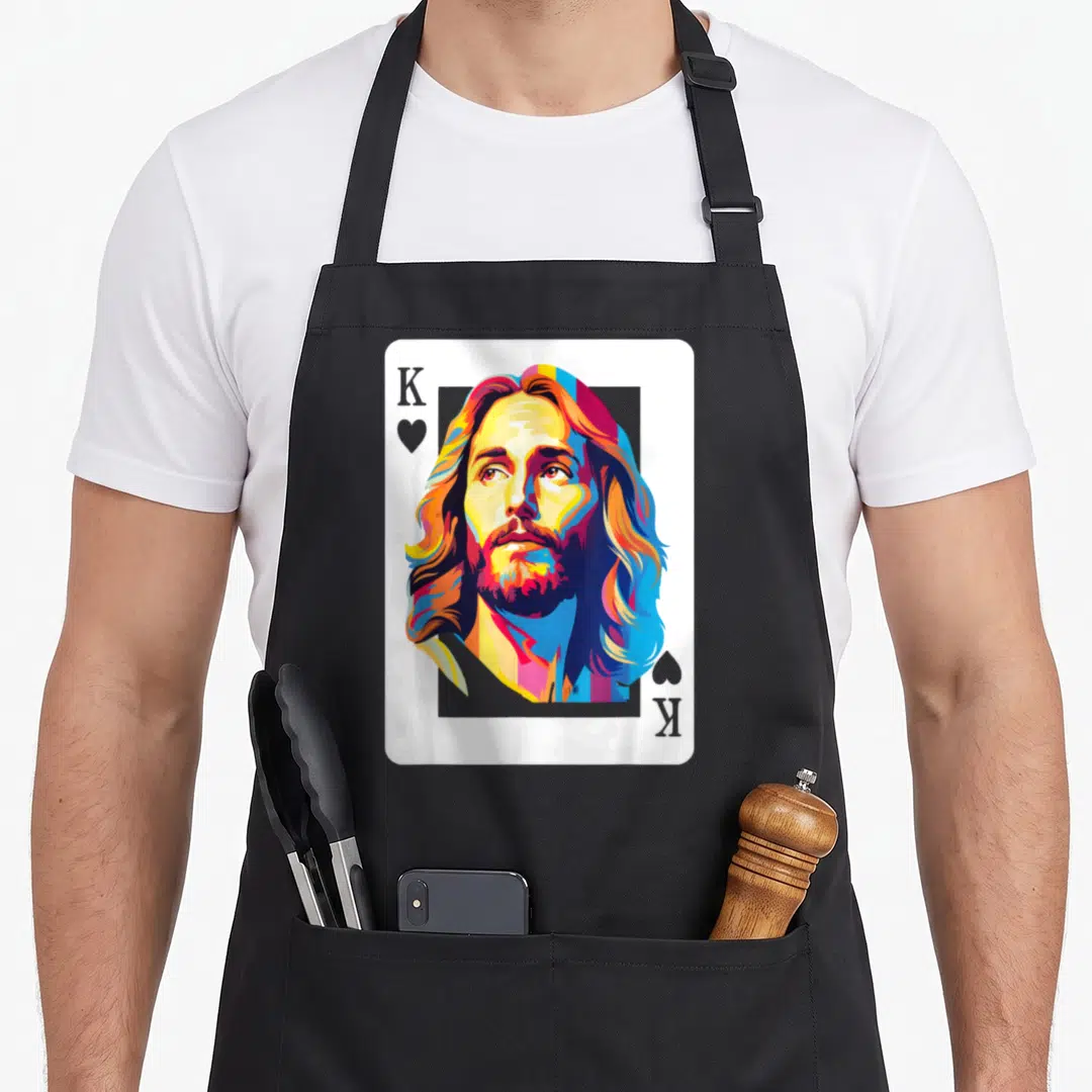 Card king of the grill apron - Colorful playing card portrait of Jesus with K and heart symbols in blue red yellow — shown on a black cotton canvas apron against a white background